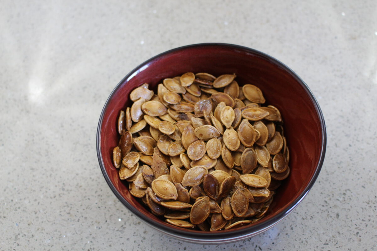 Toasted pumpkin seeds in red bowl on white counter