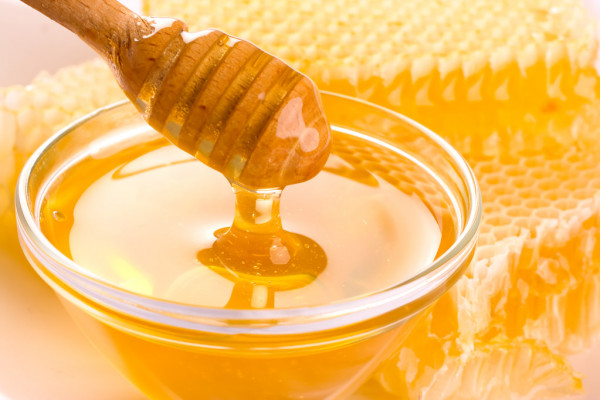 honey stick dripping with honey comb in background