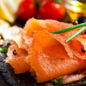 Close up view of a slate tray with smoked salmon on rustic wood table. DSRL studio photo taken with Canon EOS 5D Mk II and Canon EF 100mm f/2.8L Macro IS USM