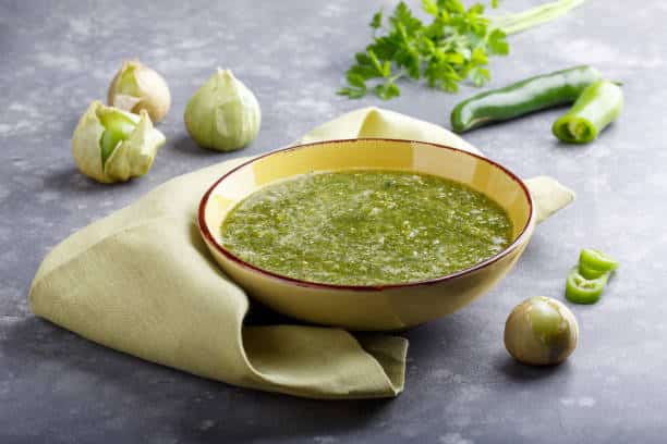 Tomatillo salsa verde. Bowl of spicy green sauce on gray table, mexican cuisine.