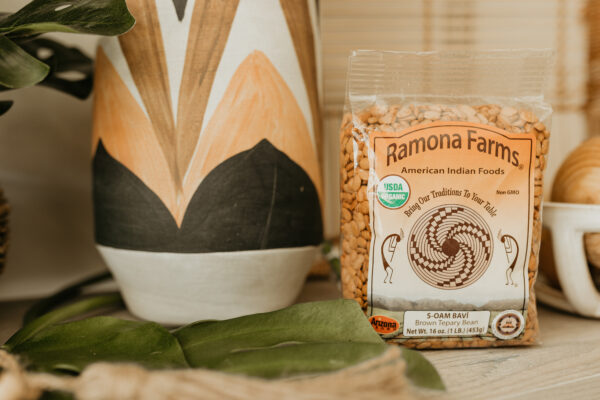 Bag of Ramona Farms brown Tepary Beans next to a white, orange and black vase and plant