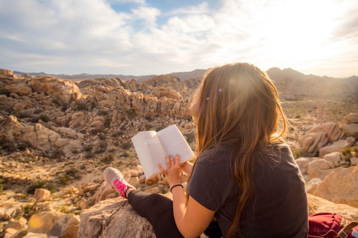 Person in black t shirt reading an unknown book sitting on a desert hill in the sunshine