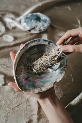 photo of the inside of an abalone shell; a sage smudge is being held near the shell