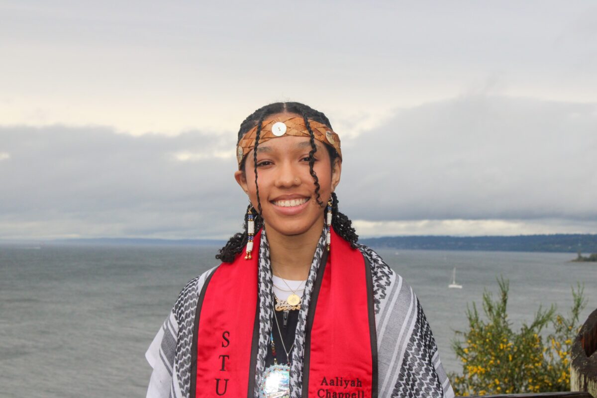 Headshot of Aaliyah Chappell with graduation sash and traditional headband with body of water in the background