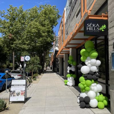 Outside view of the Seka Hills tasting room in Midtown Sacramento. The tasting room has balloons in the front door and there is a Seka Hills sign hanging just below the building's canopy. 