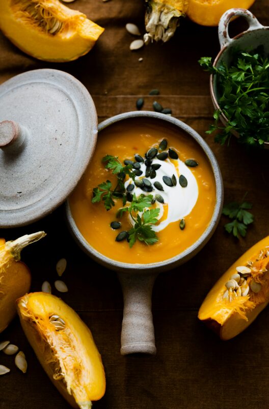 A bowl of soup with a spoon and squash on the side