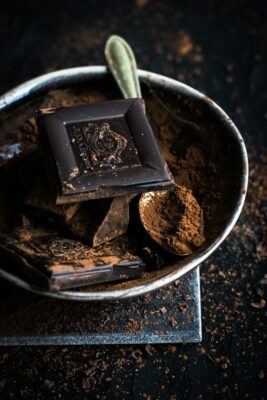 Dark chocolate bar and chocolate powder in a dark bowl with a spoon inside