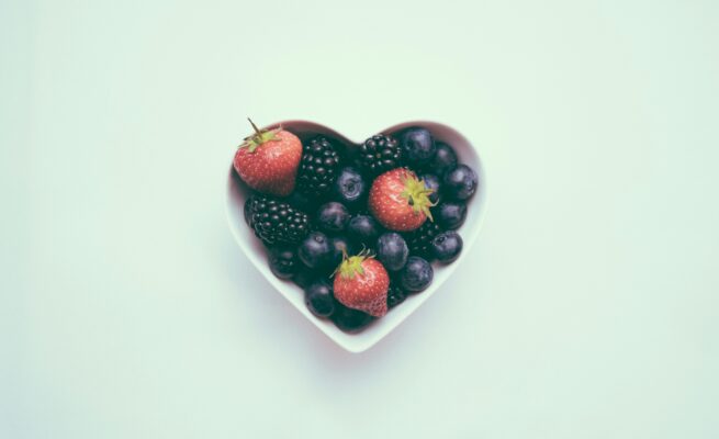 Photo of heart-shaped bowl with strawberries and blueberries against a teal green background