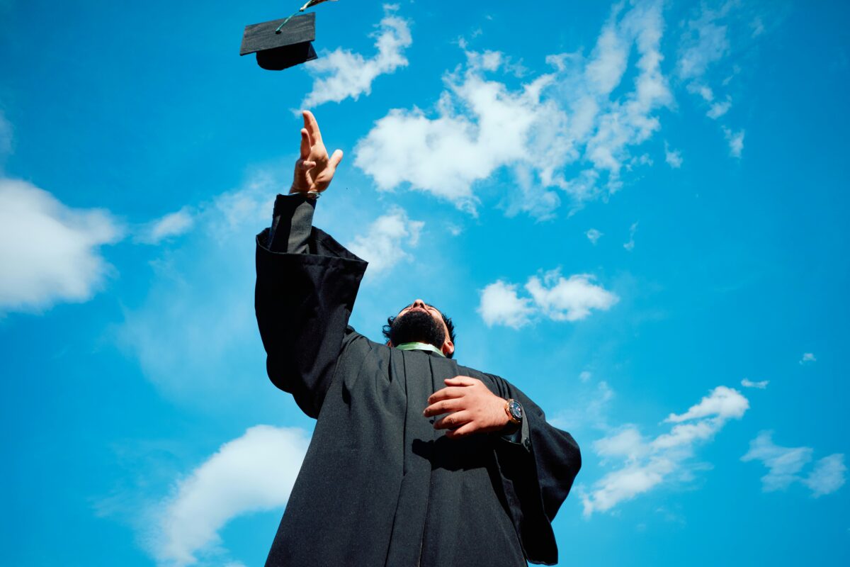Person wearing graduation gown throwing cap into the air