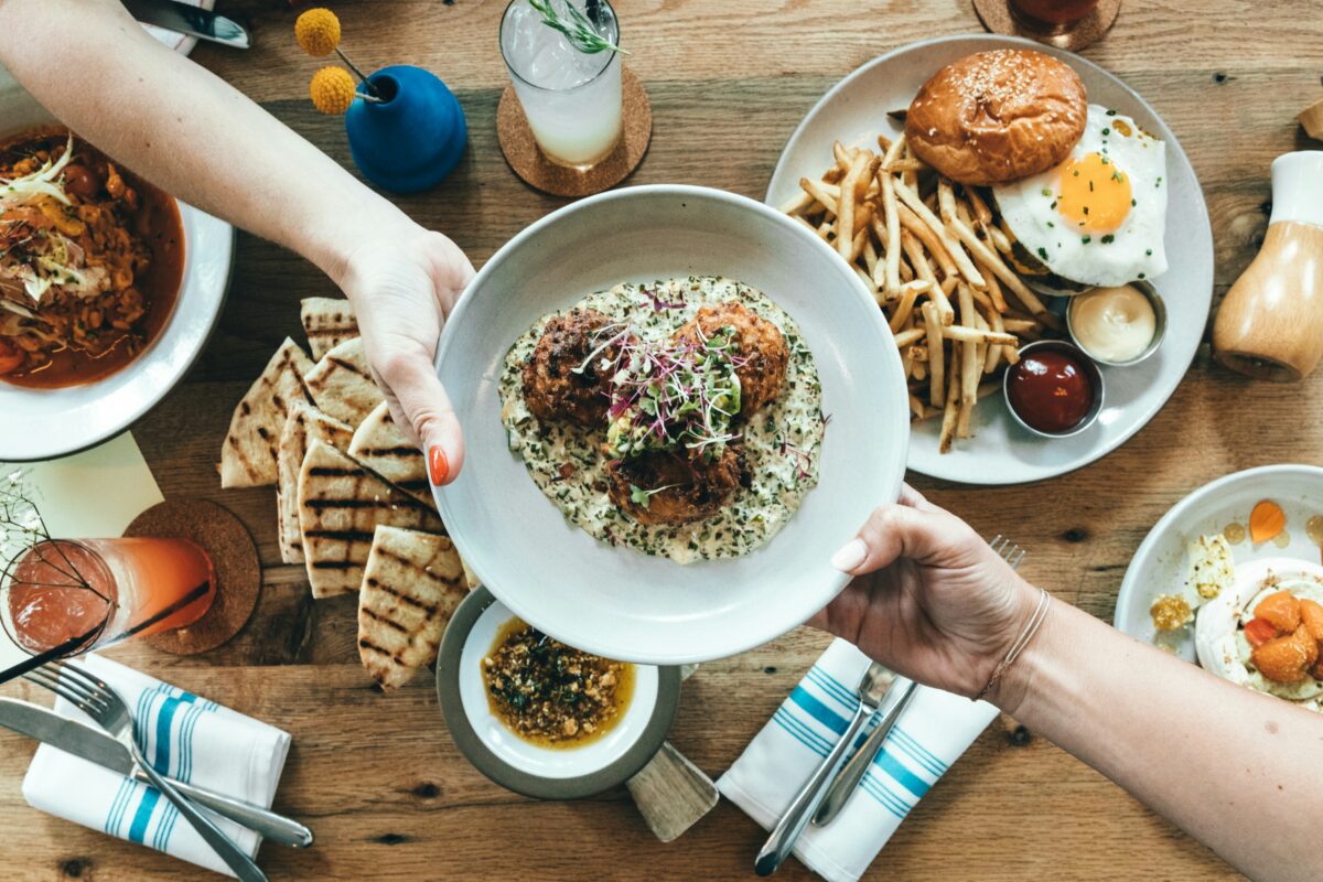 two hands reaching across a table and passing a plate of food